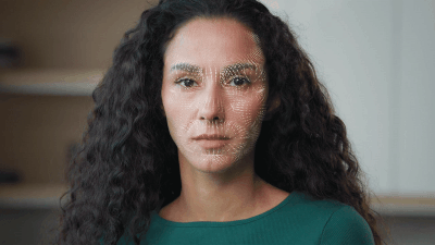 Woman with long curly hair and green top, with digital mesh overlay on her face representing facial recognition technology.