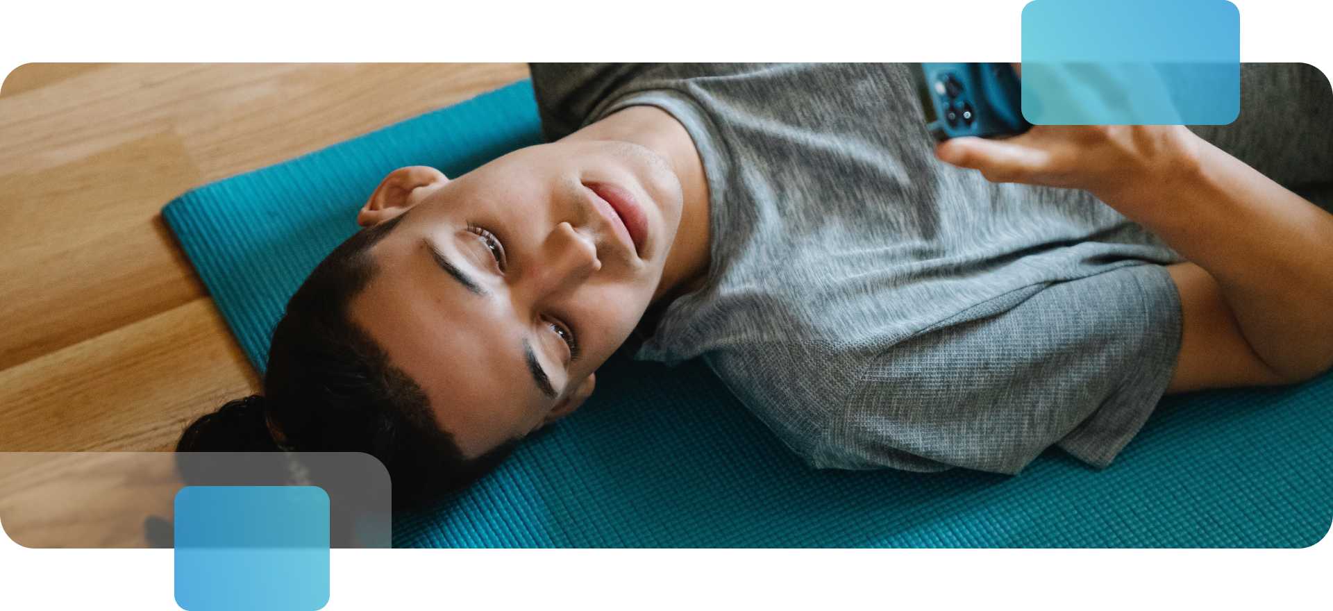 A man lying on an exercise mat holding a phone in his hand.